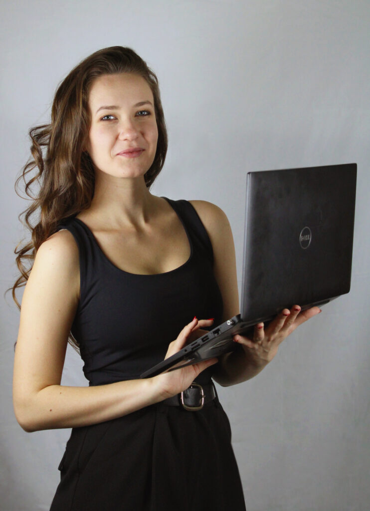 Kate, the founder of The Igniting Studio, holding a laptop and smiling confidently in a professional setting.